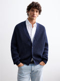 Cardigan de malha azul-marinho para homem com decote em V e fecho de botões, combinado com camisa branca, corte regular e estilo elegante para um visual casual sofisticado.