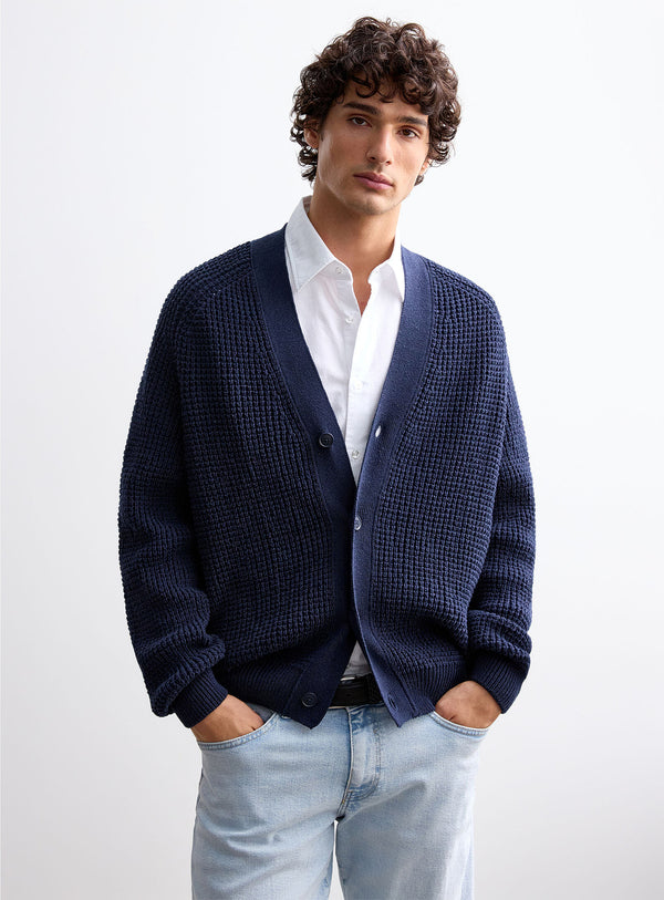 Cardigan de malha azul-marinho para homem com decote em V e fecho de botões, combinado com camisa branca, corte regular e estilo elegante para um visual casual sofisticado.