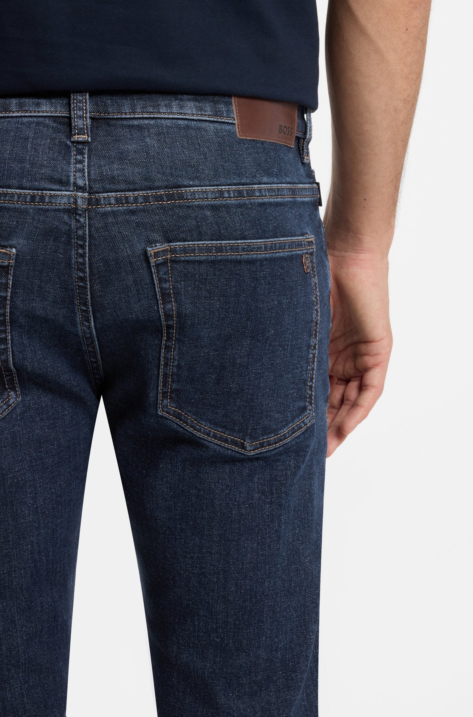 Detalhe dos bolsos traseiros das calças de ganga Delaware BOSS para homem em denim azul-escuro, com etiqueta em pele e costuras de contraste.