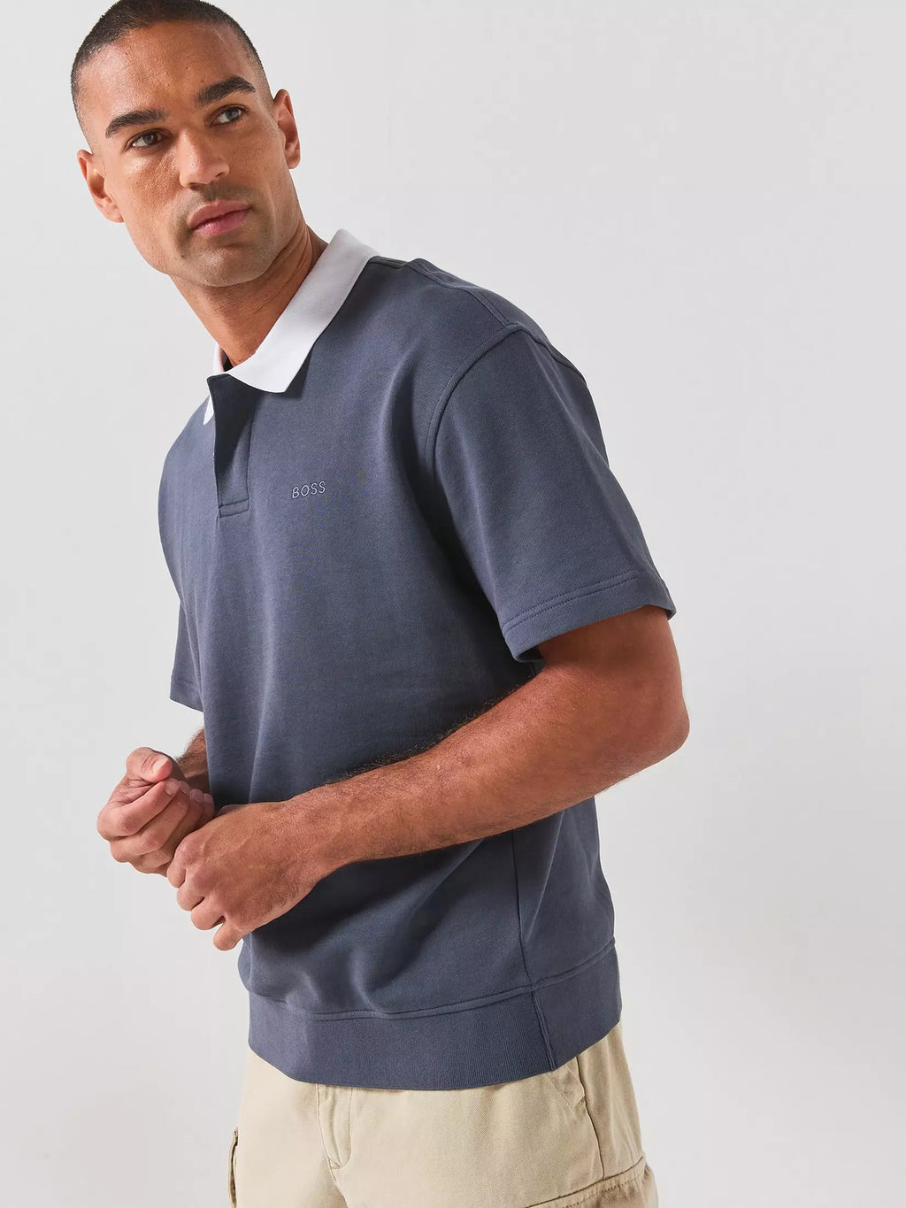 Vista lateral do polo BOSS para homem em azul-escuro, com gola branca em contraste, manga curta, logótipo BOSS bordado no peito, acabamento canelado na cintura e corte regular, evidenciando o caimento da peça e o design contemporâneo.